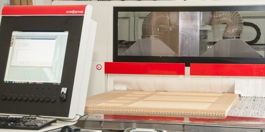 A computer sites in front of a CNC Machine, which is cutting cabinet doors