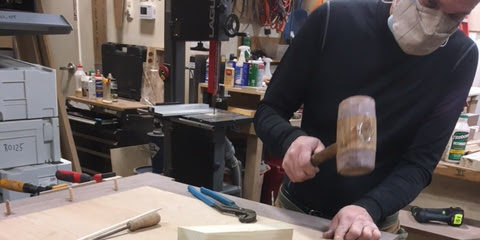 A woodworker assembles a door frame using a mallet and chisel